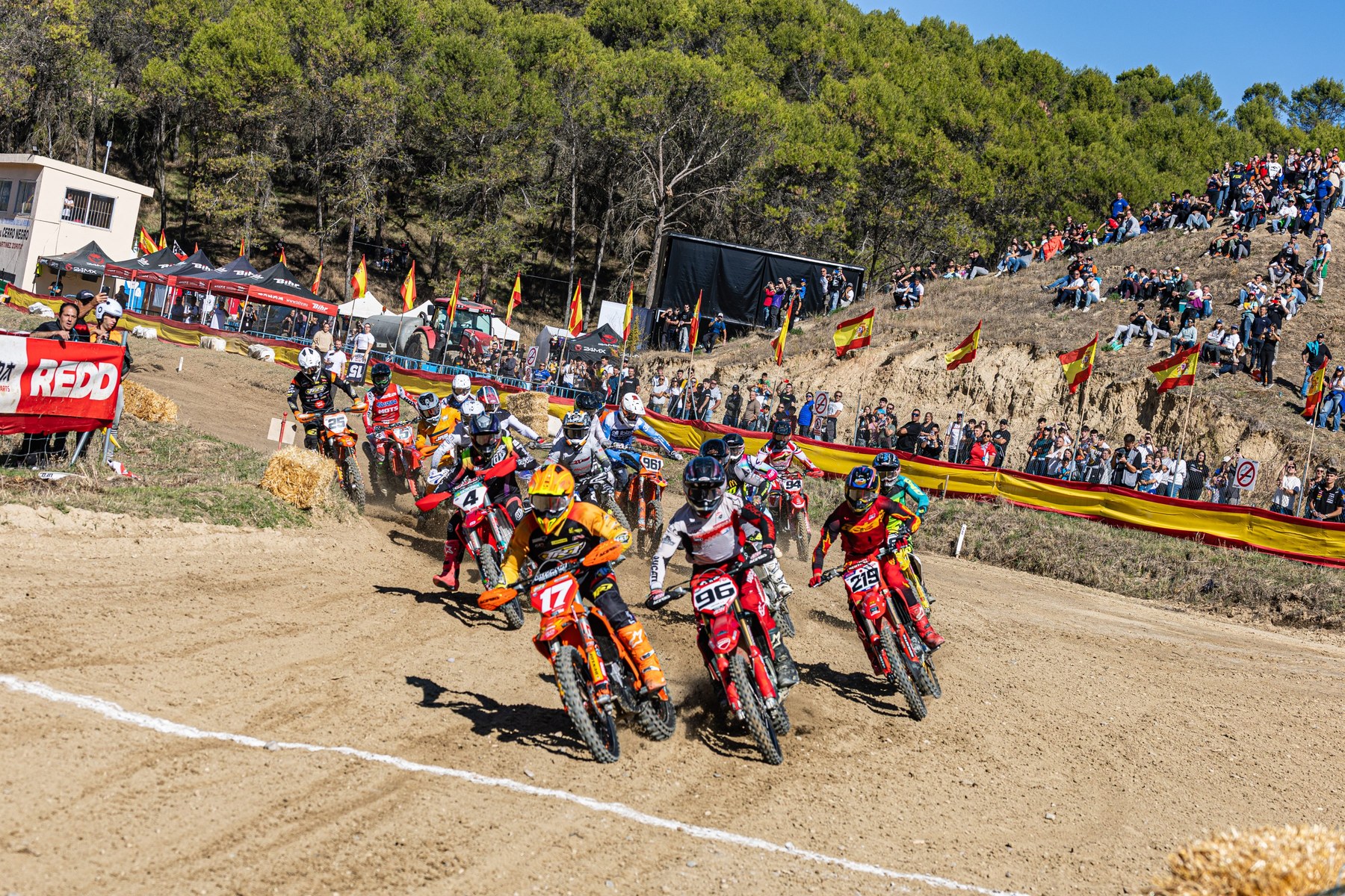 Arranque de uma manga do Campeonato de Espanha de Motocross em Talavera de la Reina: pilotos a sair da linha de partida, com bandeiras de Espanha e público ao fundo